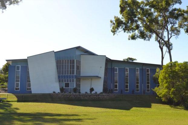 A large, modern concrete school building in blue tones with large exposed glass windows.